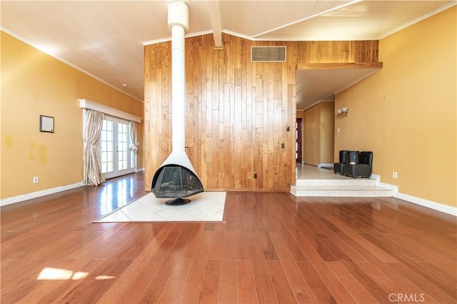 unfurnished living room with beam ceiling, french doors, wood walls, crown molding, and wood-type flooring