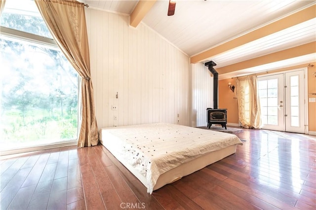 bedroom with vaulted ceiling with beams, ceiling fan, dark hardwood / wood-style flooring, and a wood stove