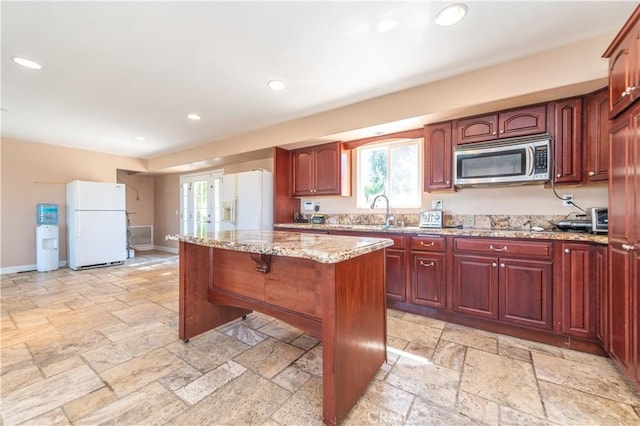 kitchen with light stone counters, sink, white refrigerator with ice dispenser, a center island, and white fridge