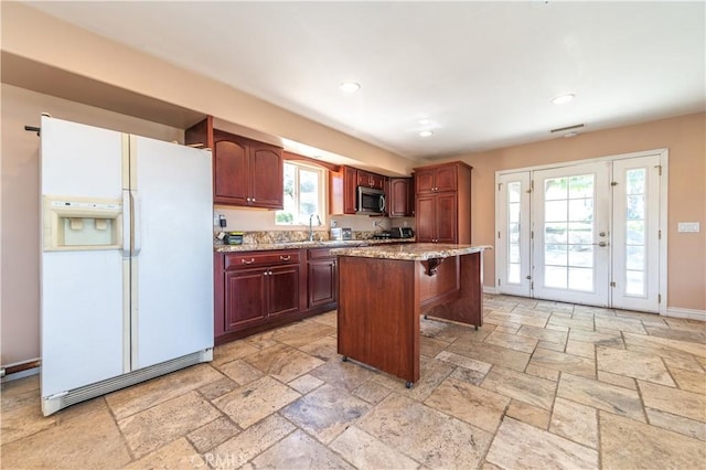 kitchen with light stone counters, a breakfast bar, sink, white refrigerator with ice dispenser, and a kitchen island