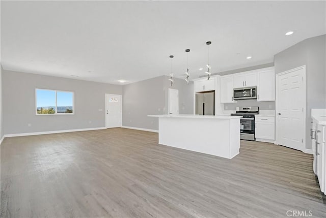 kitchen featuring white cabinetry, hanging light fixtures, stainless steel appliances, a kitchen island, and light wood-type flooring