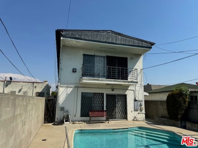 back of property with a fenced in pool, a balcony, and a patio