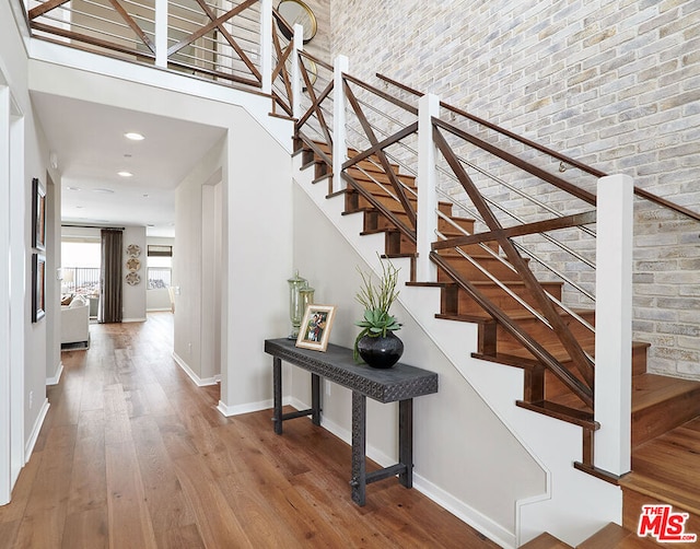 staircase featuring wood-type flooring, a towering ceiling, and brick wall