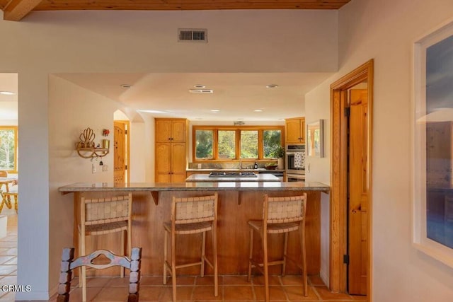 bar featuring beam ceiling, a healthy amount of sunlight, light tile patterned flooring, and stainless steel appliances