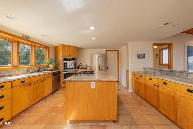 kitchen with appliances with stainless steel finishes, light stone counters, sink, light tile patterned floors, and a kitchen island