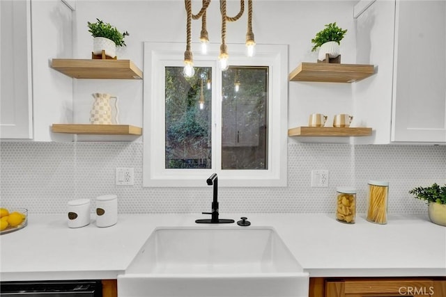 interior details featuring backsplash, sink, black dishwasher, white cabinetry, and hanging light fixtures