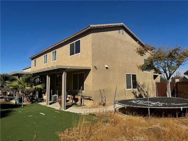 rear view of house with a patio, a trampoline, central AC unit, and a lawn