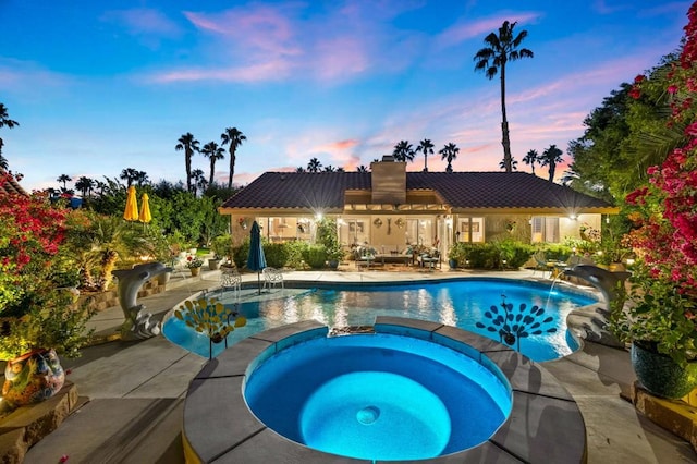 pool at dusk with an in ground hot tub and a patio