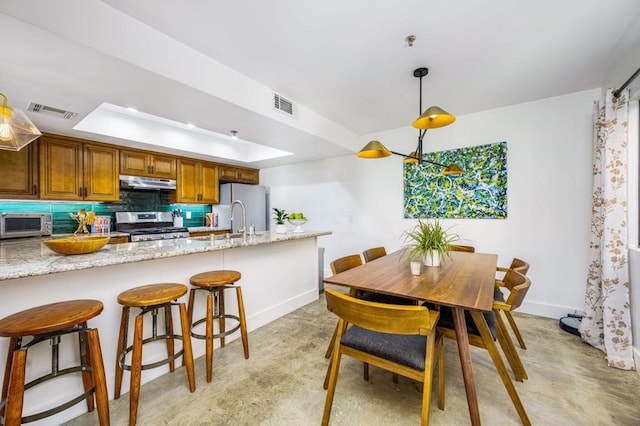 kitchen with light stone countertops, stainless steel appliances, decorative backsplash, hanging light fixtures, and a raised ceiling