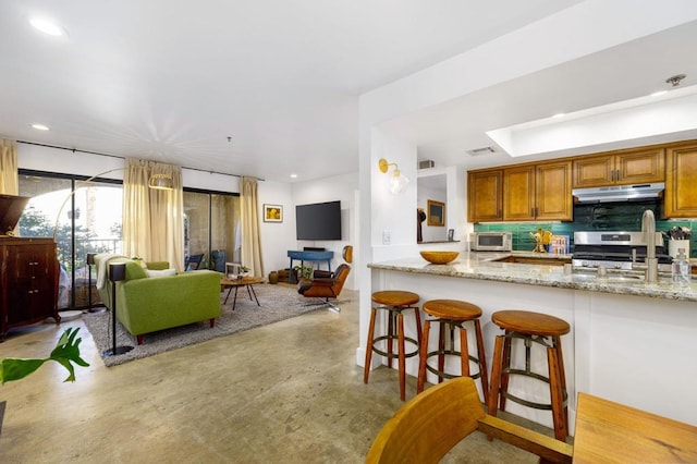 kitchen with stainless steel appliances, backsplash, a kitchen breakfast bar, light stone counters, and sink