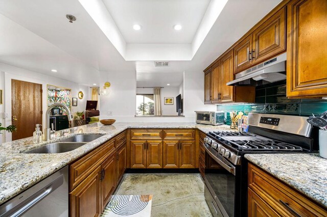 kitchen with light stone countertops, stainless steel appliances, kitchen peninsula, and sink