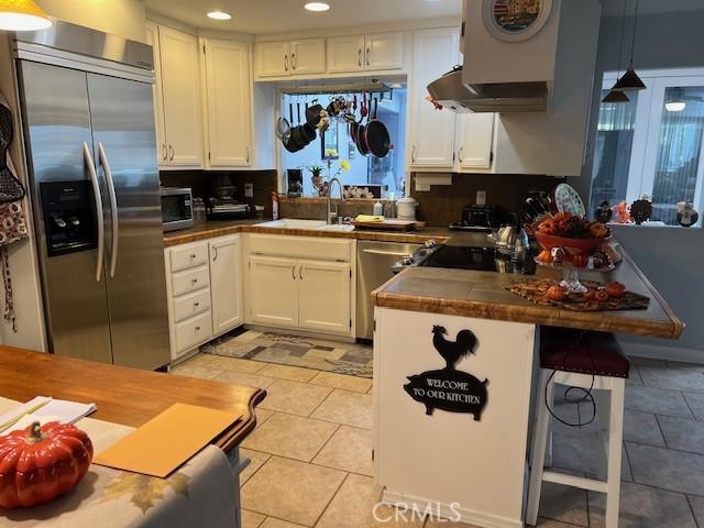 kitchen featuring white cabinetry, sink, kitchen peninsula, decorative light fixtures, and appliances with stainless steel finishes