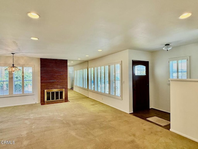 carpeted entryway featuring a brick fireplace, a wealth of natural light, and a notable chandelier