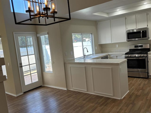 kitchen featuring white cabinets, sink, decorative light fixtures, kitchen peninsula, and stainless steel appliances