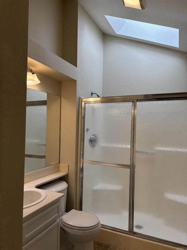 bathroom with a skylight, a shower with door, vanity, and toilet