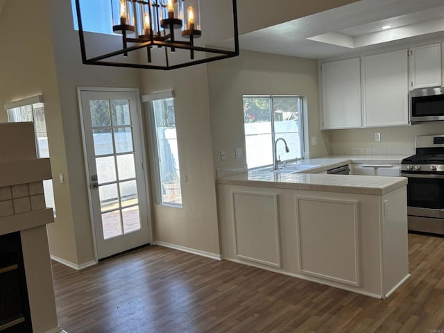 kitchen featuring sink, dark wood-type flooring, kitchen peninsula, white cabinets, and appliances with stainless steel finishes