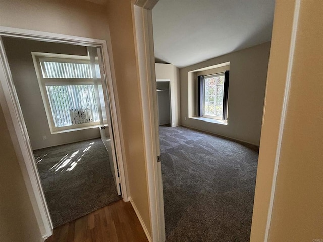 hallway with dark colored carpet and vaulted ceiling