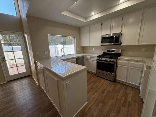 kitchen featuring kitchen peninsula, tile counters, white cabinets, and appliances with stainless steel finishes