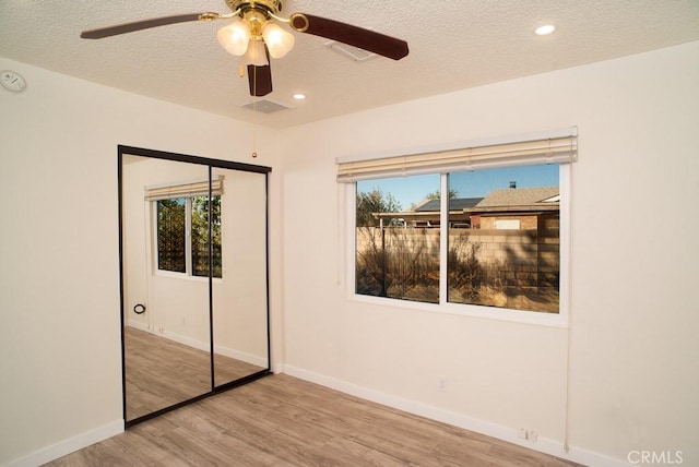 unfurnished bedroom featuring a textured ceiling, light hardwood / wood-style flooring, a closet, and ceiling fan