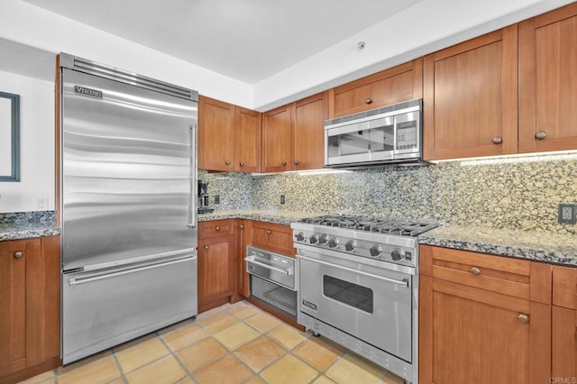 kitchen featuring light stone counters, light tile patterned floors, decorative backsplash, and high quality appliances