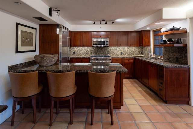 kitchen featuring dark stone counters, sink, pendant lighting, stainless steel appliances, and a breakfast bar area