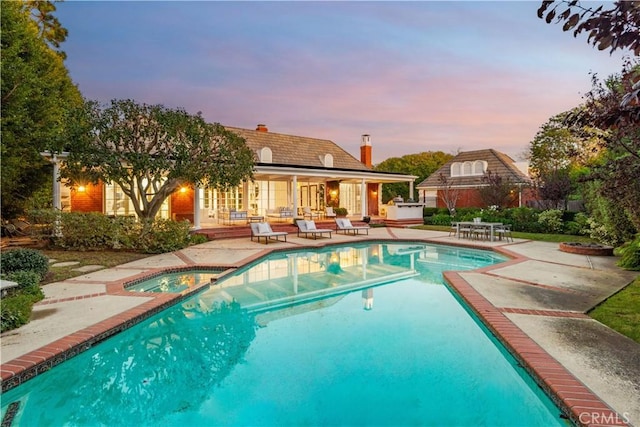 pool at dusk with a patio area and an in ground hot tub