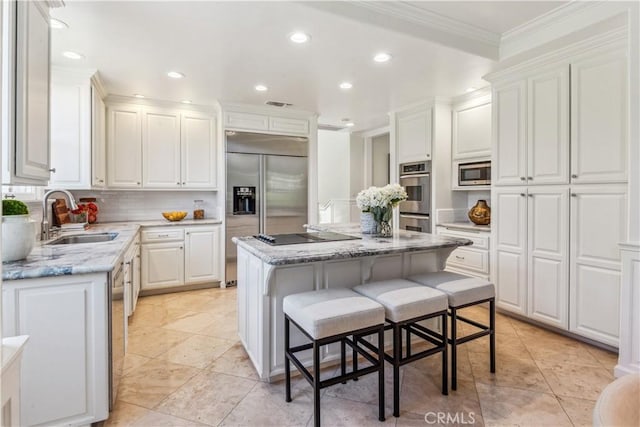 kitchen featuring a breakfast bar, a center island, sink, built in appliances, and white cabinetry