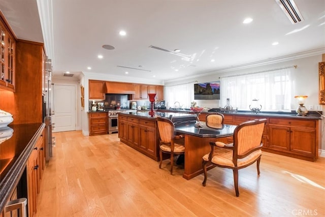 kitchen featuring a breakfast bar, light hardwood / wood-style flooring, ornamental molding, and an island with sink