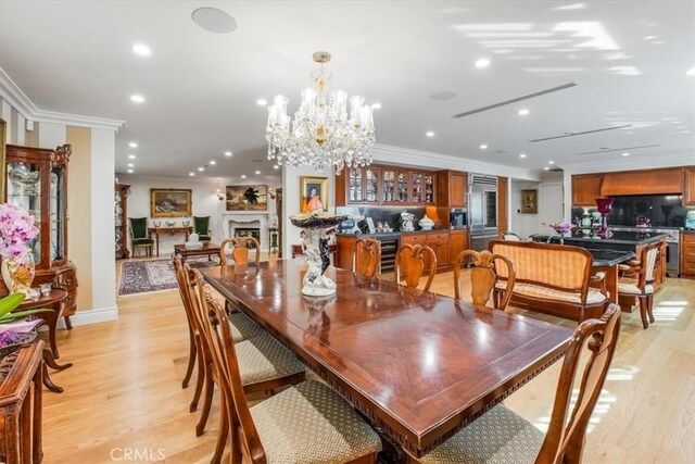 dining area with a notable chandelier, light hardwood / wood-style floors, crown molding, and beverage cooler