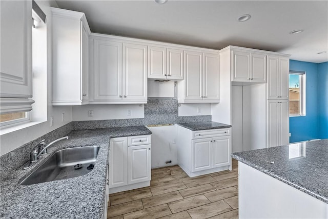 kitchen with white cabinetry, a healthy amount of sunlight, dark stone countertops, and sink