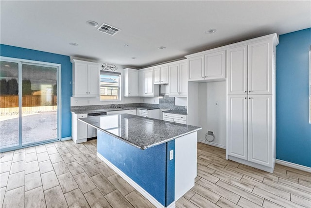 kitchen featuring dishwasher, a kitchen island, white cabinetry, dark stone countertops, and sink