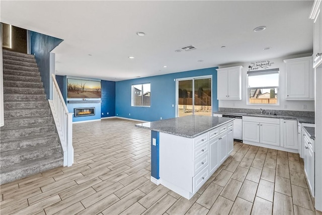 kitchen with a kitchen island, dark stone countertops, stainless steel dishwasher, and white cabinetry