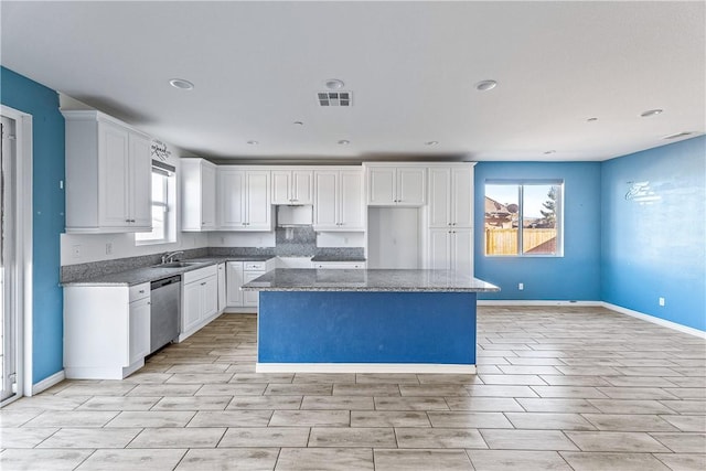 kitchen with dark stone countertops, a center island, stainless steel dishwasher, sink, and white cabinetry