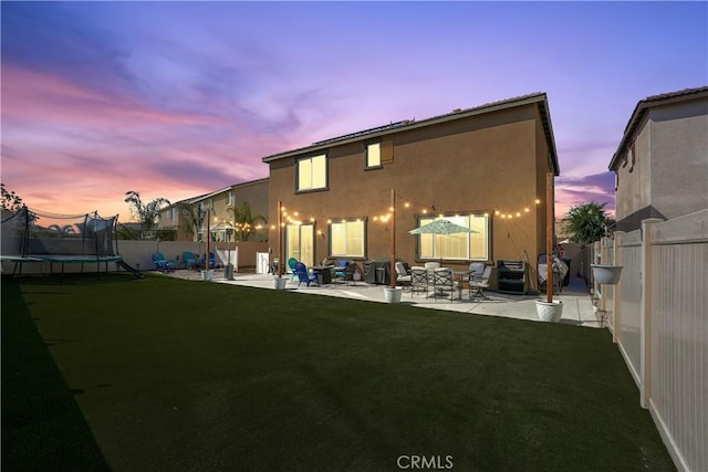 back house at dusk featuring a lawn, a patio, and a trampoline