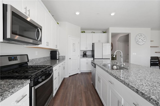 kitchen with appliances with stainless steel finishes, light stone counters, dark wood-type flooring, sink, and white cabinets