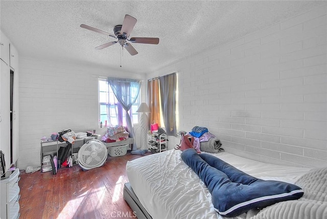 bedroom featuring hardwood / wood-style flooring, ceiling fan, brick wall, and a textured ceiling