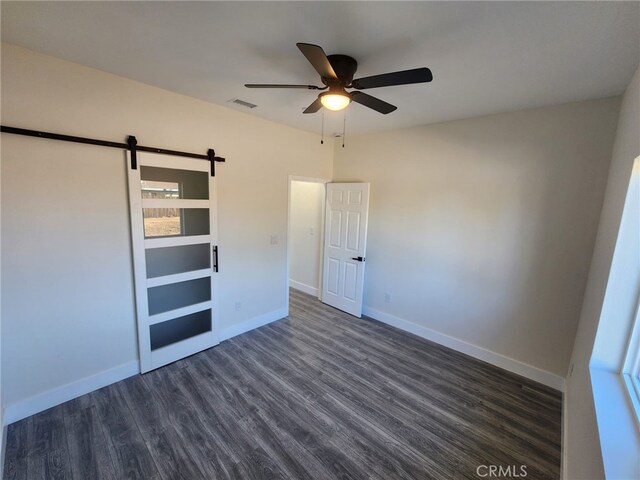 unfurnished bedroom featuring ceiling fan, dark hardwood / wood-style flooring, and a barn door