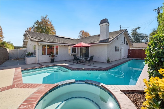 back of property featuring a patio and a swimming pool with hot tub