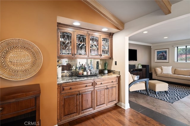 bar with dark stone countertops, crown molding, vaulted ceiling with beams, and dark hardwood / wood-style floors