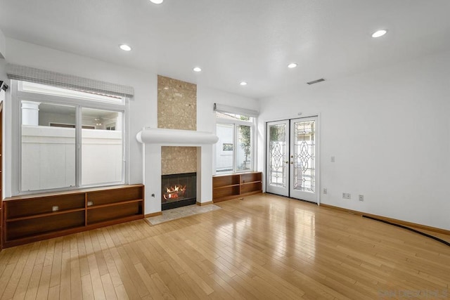 unfurnished living room with french doors, light wood-type flooring, and a tiled fireplace