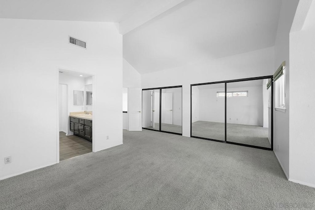 unfurnished bedroom featuring light carpet, high vaulted ceiling, two closets, sink, and ensuite bath