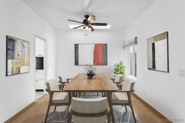 dining area featuring ceiling fan, light wood-type flooring, and a skylight