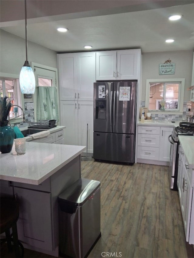 kitchen featuring hardwood / wood-style floors, backsplash, white cabinets, decorative light fixtures, and stainless steel appliances