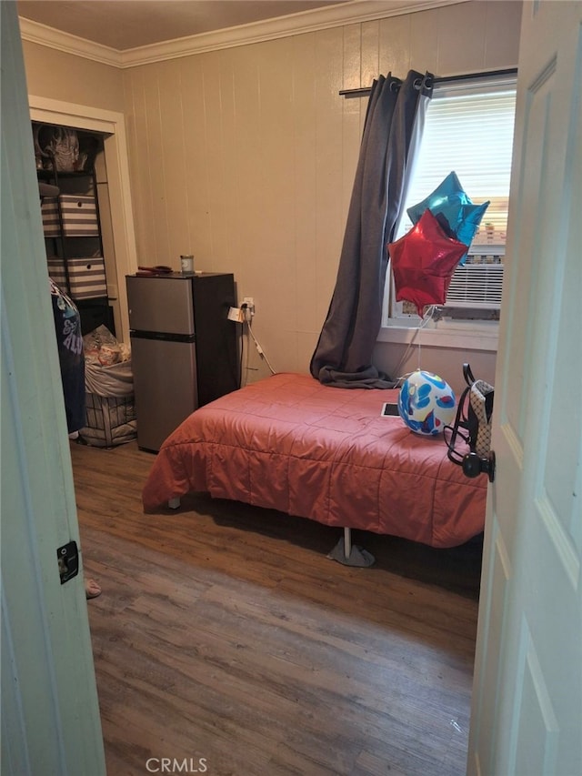 bedroom with cooling unit, wooden walls, stainless steel fridge, ornamental molding, and wood-type flooring