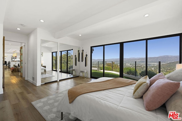 bedroom with beamed ceiling, wood-type flooring, a mountain view, and access to exterior