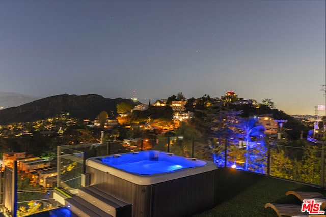 pool at dusk featuring a hot tub and a mountain view