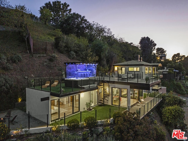 back house at dusk with outdoor lounge area, a patio area, and a lawn