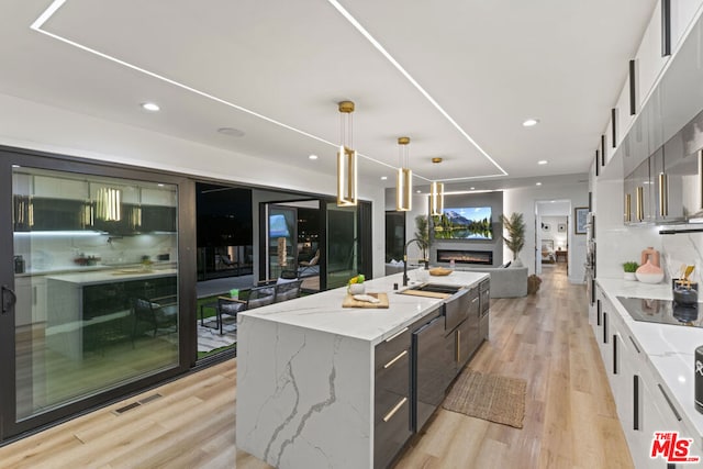 kitchen featuring white cabinetry, light stone counters, decorative light fixtures, an island with sink, and black electric stovetop