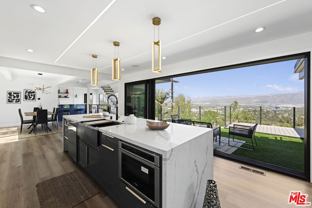 kitchen with pendant lighting, sink, a kitchen island with sink, a mountain view, and light wood-type flooring