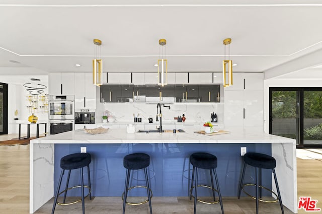 kitchen featuring a center island with sink, sink, pendant lighting, and stainless steel double oven